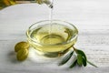 Pouring of olive oil from bottle into glass bowl on wooden table Royalty Free Stock Photo