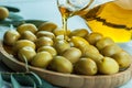 Pouring olive oil from bottle into glass on raw turkish green olives in bamboo bowl Royalty Free Stock Photo