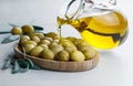 Pouring olive oil from bottle into glass on raw turkish green olives in bamboo bowl Royalty Free Stock Photo