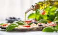 Pouring olive oil on caprese salad. Healthy italian or mediterranean meal