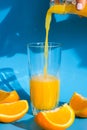 Pouring orange juice stream from jug into glass of squeezing Orange juice with sliced fruits on blue background. Fruit Royalty Free Stock Photo