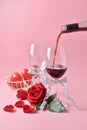 Pouring out of red wine from bottle to glass, with rose at the bottom on pink background. Concept of Valentine`s Day Royalty Free Stock Photo