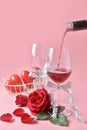 Pouring out of red wine from bottle to glass, with rose at the bottom on pink background. Concept of Valentine`s Day Royalty Free Stock Photo