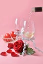 Pouring out of white wine from bottle to glass, with rose at the bottom on pink background. Concept of Valentine`s Day, pop art c Royalty Free Stock Photo