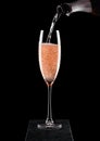 Pouring pink rose champagne from bottle to glass on black marble board on black background. Space for text Royalty Free Stock Photo