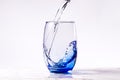 Pouring purified drinking water into a blue glass, white background carrara marble base. empty glass