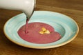 Pouring raspberry cream soup into a bowl on a wooden table Royalty Free Stock Photo