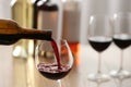 Pouring red wine from bottle into glass on blurred background, closeup. Space for text Royalty Free Stock Photo