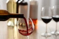 Pouring red wine from bottle into glass on blurred background, closeup. Space for text Royalty Free Stock Photo