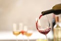 Pouring red wine from bottle into glass on blurred background. Royalty Free Stock Photo