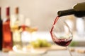 Pouring red wine from bottle into glass on blurred background Royalty Free Stock Photo