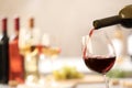 Pouring red wine from bottle into glass on blurred background. Royalty Free Stock Photo