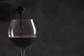 Pouring red wine from bottle into glass on dark background, closeup. Space for text Royalty Free Stock Photo