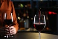 Pouring red wine from bottle into glass on table indoors, closeup. Space for text Royalty Free Stock Photo