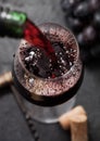Pouring red wine from bottle to glass on black background with corks and corkscrew Royalty Free Stock Photo