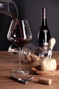 Pouring red wine in crystal glass, bottle, corkscrew, opener, sommelier knife, transparent decanter, corks, cheese on wooden table Royalty Free Stock Photo