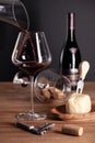 Pouring red wine in crystal glass, bottle, corkscrew, opener, sommelier knife, transparent decanter, corks, cheese on Royalty Free Stock Photo