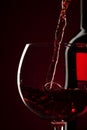 Pouring red wine into the glass against red black background Royalty Free Stock Photo