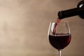 Pouring red wine into glass from bottle against blurred beige background, closeup Royalty Free Stock Photo