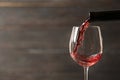 Pouring red wine into glass from bottle against blurred wooden background, closeup Royalty Free Stock Photo