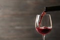 Pouring red wine into glass from bottle against blurred wooden background, closeup Royalty Free Stock Photo