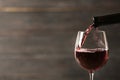 Pouring red wine into glass from bottle against blurred wooden background. Space for text Royalty Free Stock Photo