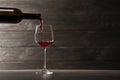 Pouring red wine into glass from bottle on table against wooden background Royalty Free Stock Photo