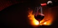 Pouring red wine into a glass at night near fireplace flames. Cozy wintertime background with copy space