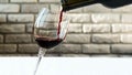 Pouring red wine into a wine glass against a brick wall background,pouring bottle wine into a glass,close-up. Royalty Free Stock Photo