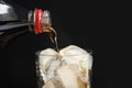 Pouring refreshing cola from bottle into glass with ice cubes on black background Royalty Free Stock Photo