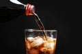 Pouring refreshing cola from bottle into glass with ice cubes on black background Royalty Free Stock Photo