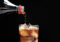 Pouring refreshing cola from bottle into glass with ice cubes on black background Royalty Free Stock Photo