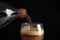 Pouring refreshing cola from bottle into glass with ice cubes on black background Royalty Free Stock Photo