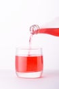 Pouring a refreshing red bubbly soda drink from bottle into glass on white background closeup Royalty Free Stock Photo