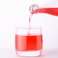 Pouring a refreshing red bubbly soda drink from bottle into glass on white background closeup Royalty Free Stock Photo