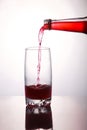 Pouring a refreshing red bubbly soda drink from bottle into glass on white background closeup with reflections Royalty Free Stock Photo