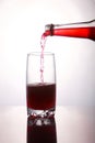 Pouring a refreshing red bubbly soda drink from bottle into glass on white background closeup with reflections Royalty Free Stock Photo