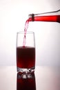 Pouring a refreshing red bubbly soda drink from bottle into glass on white background closeup with reflections Royalty Free Stock Photo