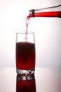 Pouring a refreshing red bubbly soda drink from bottle into glass on white background closeup with reflections Royalty Free Stock Photo