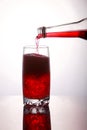 Pouring a refreshing red bubbly soda drink from bottle into glass on white background closeup with reflections Royalty Free Stock Photo