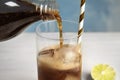 Pouring refreshing soda drink into glass with ice cubes and straw on table Royalty Free Stock Photo