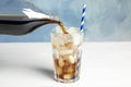 Pouring refreshing soda drink into glass with ice cubes on wooden table against blue background Royalty Free Stock Photo