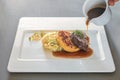 Pouring sauce on a dish from roast venison, flat bread dumpling and round shaped cabbage vegetable on a white plate, preparation Royalty Free Stock Photo