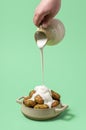 Pouring sour cream over roasted potatoes, minimalist on a green background