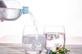 Pouring of sparkling soda mineral drink water in glasses with ice cubes close up copy space