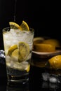 Pouring Sparkling water or other transparent drink with a lemons slices and ice cubes in Beautiful glass on black background