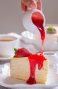 Pouring strawberry sauce onto delicious crepe cake on white plate