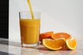 Pouring stream of fresh orange juice into glass and cut oranges on the table Royalty Free Stock Photo