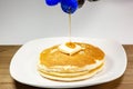 Pouring syrup from a blue tip bottle onto the square of butter on a stack of golden pancakes waiting to be eaten Royalty Free Stock Photo