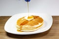 Pouring syrup from a blue tip bottle onto the square of butter on a stack of golden pancakes waiting to be eaten Royalty Free Stock Photo